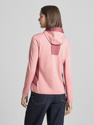 Frauenmodel trägt Jacke mit Logo-Stitching von PEAK PERFORMANCE in Rosa, Elastischer-Material-Mix, körpernahe Passform, Kapuze, Reißverschluss, Brusttasche mit Reißverschluss, Logo-Stitching, Ganzkörperansicht Rückansicht.