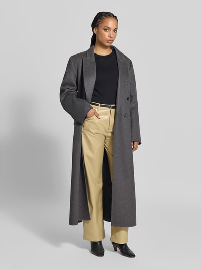 Frauenmodel trägt Relaxed Fit Mantel aus Schurwoll-Mix von Victoria Beckham in Dunkelgrau, Reverskragen, doppelte Knopfleiste, Pattentaschen, glatte Textur, Kombi mit heller Hose und schwarzem Oberteil, Ganzkörperansicht von vorne.