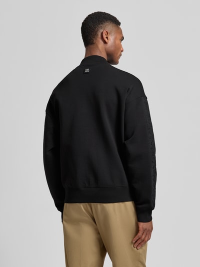 Männermodel trägt Oversized Sweatjacke aus Baumwoll-Mix Modell 'Dromzip' von HUGO in Schwarz mit College-Kragen, Rückansicht