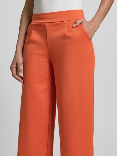 Kobiece modelki noszą spodnie materiałowe Wide Fit Stoffhose mit Viskose-Anteil Modell 'Kate' od ICHI, elastyczna mieszanka materiałów z dodatkiem wiskozy, zakładki w pasie, intensywnie pomarańczowy kolor, tekstura gładka, widoczny elastyczny pas, długość wewnętrzna nogawki 79 cm, szerokość pasa 38 cm, detailaufnahme.