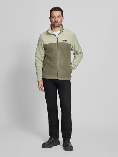 Männermodel trägt Regular Fit Fleecejacke mit Logo-Patch Modell 'Mountain' von COLUMBIA in Grün mit Stehkragen und Reißverschluss, Eingrifftaschen, elastische Ärmelabschlüsse, Rückenlänge 70 cm, Ärmellänge 68 cm; Ganzkörperansicht von vorne.