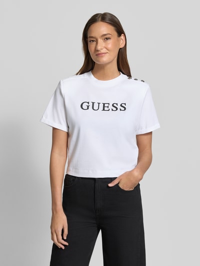 Vrouwenmodel draagt Cropped T-shirt met Logo model 'MARINA' van Guess, puur katoen, korte fit, ronde hals, logoprint, ruglengte maat S 45 cm. Ganzkörperansicht von voren.