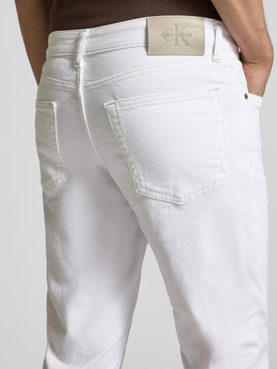 Mężczyzna nosi Slim Fit Jeans mit Eingrifftaschen od Calvin Klein Jeans z bawełnianym materiałem, białe, detal tylnej kieszeni, krój slim fit, szerokość w rozmiarze 32/32: 43 cm, długość nogawki wewnętrznej: 78 cm, detal tylu.