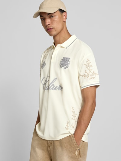 Männermodel trägt Poloshirt floralem Allover-Stitching von Don´t Waste Culture in Creme mit Logo-Print, Relaxed-Fit, Polokragen, Kurzärmelig, Rückenlänge 71 cm bei Größe M, Ganzkörperansicht von vorne.