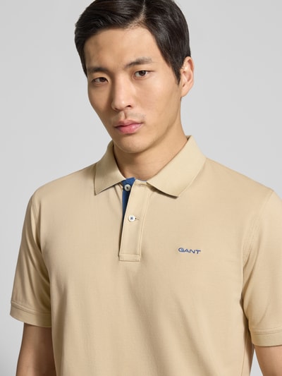 Männermodel trägt Regular Fit Poloshirt mit Logo-Stitching von Gant aus beigem Baumwoll-Mix mit Polokragen, Nahaufnahme Oberkörper.