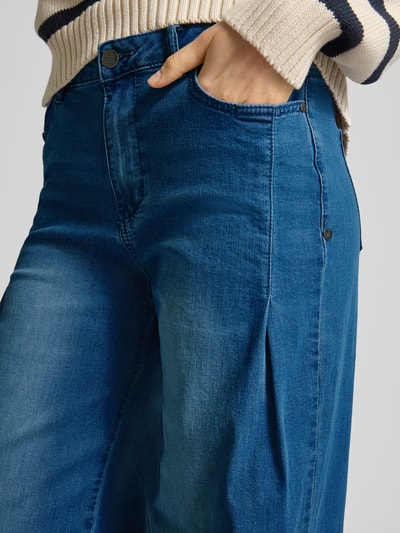Vrouwenmodel draagt Wide Fit Jeans met Lyocell-Viskose-Anteil van Buena Vista, mix van katoen, lyocell en viscose, 5-pocketmodel, knoop- en ritssluiting, bandwijdte maat S 40 cm, binnenbeenlengte 81 cm, middenblauwe kleur met zichtbare textuur, detailopname heup.