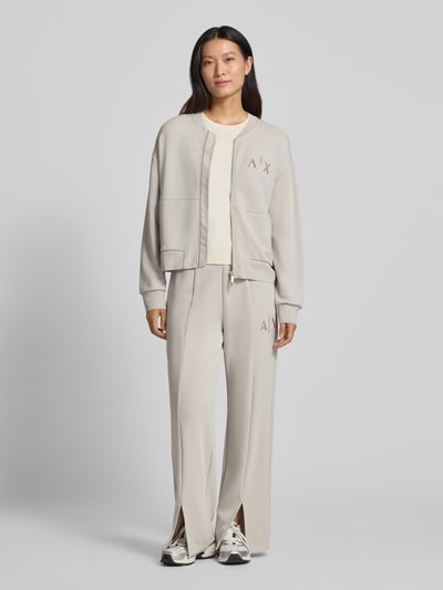 Vrouwenmodel draagt Straight Fit Sweatpants uit elastische viscosemix van Armani Exchange in lichtbeige met labeldetail, pijpsplitten, elastische band, binnenbeenlengte maat S: 77 cm, comfortlook, volledige lichaamsvooraanzicht.