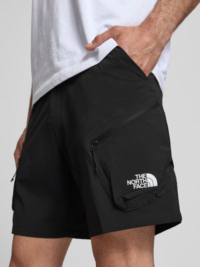 Männermodel trägt Shorts mit Cargotaschen und Logo von The North Face aus schwarzem Material-Mix mit Stretch-Anteil, Nahaufnahme Oberschenkel.