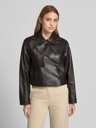 Kobiecy model nosi Regular Fit Lederjacke aus echtem Lammleder Modell 'SARCAE' od BOSS, czarny matowy kolor, długi rękaw, krój regular fit, zapięcie na napy, kołnierz z klapami, skórzana faktura, boczne kieszenie, elastyczne wykończenia, widok całej sylwetki z przodu.