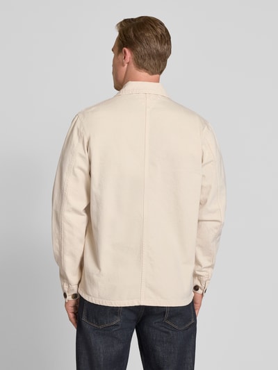 Męski model nosi Regular Fit Hemdjacke aus reiner Baumwolle od Tommy Hilfiger, efekt: jednolity kolor, tkanina stylizowana na denim, wykładany kołnierz, listwa guzikowa, wyhaftowane logo, długi rękaw z mankietami, nakładana kieszeń na piersi i wpuszczane kieszenie, wykończenie materiału: rigid denim, bawełna, jasny beż, Ganzkörperansicht Rückansicht.