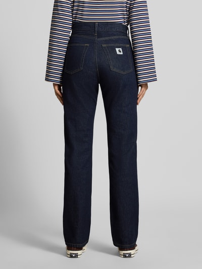 Frauenmodel trägt Slim Fit Jeans mit Knopfverschluss Modell 'Noxon' von Carhartt Work In Progress, dunkles Denim, 5-Pocket-Design, Ganzkörperansicht Rückansicht.