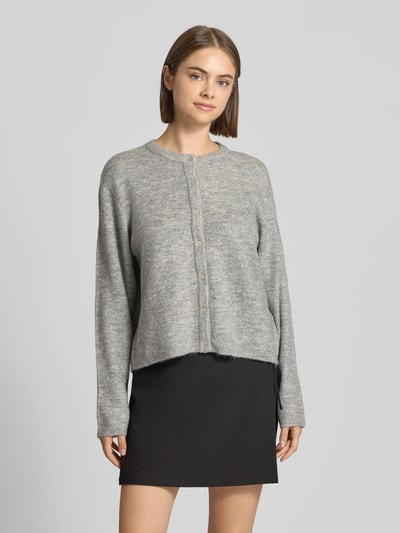 Frauenmodel trägt Loose Fit Strickjacke mit Rundhalsausschnitt Modell 'SIMONI' von ONLY, graue Farbe, Damen Strickjacke, Ganzkörperansicht von vorne.