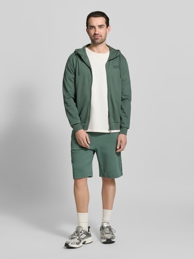 Männermodel trägt grüne Shorts mit elastischem Bund von EA7 Emporio Armani aus Baumwoll-Mix, Regular Fit, Ganzkörperansicht von vorne.