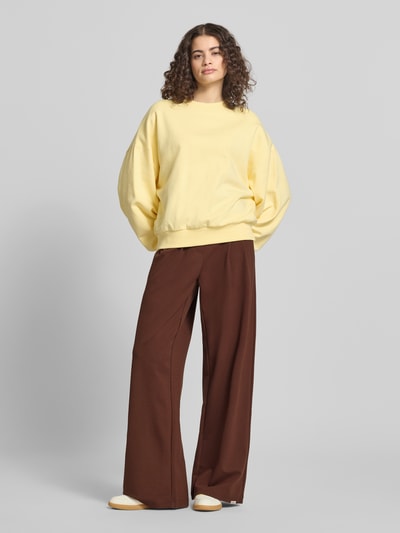 Frauenmodel trägt Wide Fit Stoffhose aus Viskose-Mix Modell 'Miri' von OH APRIL in Braun, elastischer Bund, Bundfalten, Ganzkörperansicht von vorne