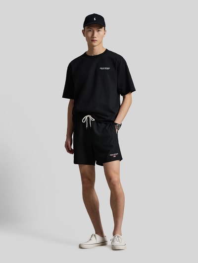 Männermodel trägt Badeshorts mit Label Stitching von Polo Ralph Lauren in Schwarz, unifarben mit Tunnelzug und Seitentaschen, Ganzkörperansicht von vorne.