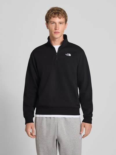 Männermodel trägt Regular Fit Sweatshirt mit Troyer Modell "EVOLUTION" van The North Face, katoenmix, logostitching, zwart, ganzkörperaanzicht van voren. Ruglengte bij maat M: 67 cm, mouwlengte bij maat M: 68 cm.