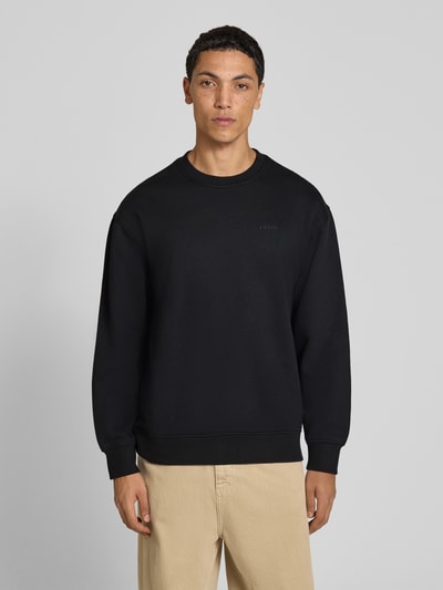 Männermodel trägt schwarzes Relaxed Fit Sweatshirt aus Baumwoll-Mix von Levi's®, helle Hose, neutraler Hintergrund, Ganzkörperansicht von vorne.