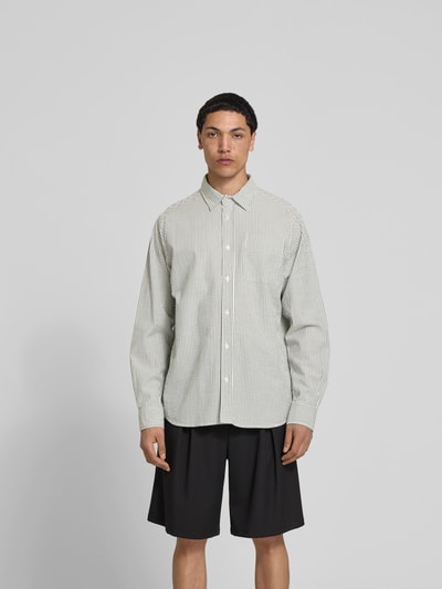 Männermodel trägt Relaxed Fit Freizeithemd mit Brusttasche von Forét, gestreiftes Baumwollhemd, Kentkragen, Langarm, Ganzkörperansicht von vorne.