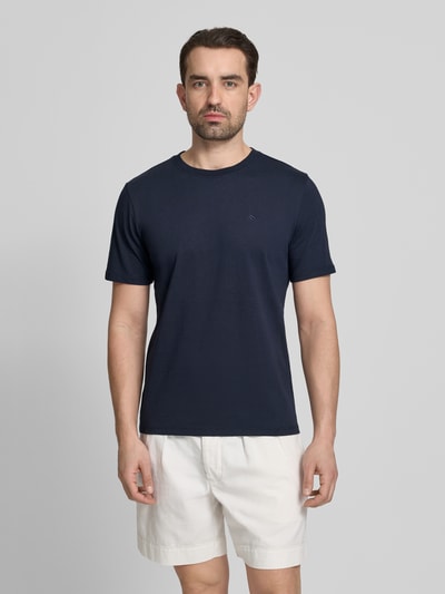 Männermodel trägt T-Shirt mit Label-Stitching und Rundhalsausschnitt von Scotch & Soda, Reine Baumwolle, Regular-Fit, Herren T-Shirt, Rückenlänge 68 cm, Größe M, dunkelblau, weiße Shorts, Ganzkörperansicht von vorne.