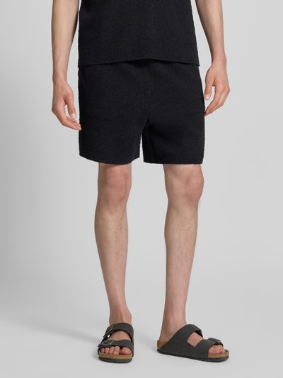Männermodel trägt Relaxed Fit Sweatshorts aus Baumwoll-Mix von Lacoste in Schwarz, unifarben, Bouclé-Textur, Nahaufnahme Oberkörper bis Knie.