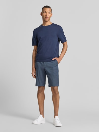 Männermodel trägt Bermudas mit Gürtel und Gesäßleistentaschen von Christian Berg Men aus Baumwoll-Mix mit Stretch-Anteil in Blau, Ganzkörperansicht von vorne. Passform: Straight Fit; Details: Knopf- und Reißverschluss, Gürtel, französische Eingrifftaschen; Bundweite bei Größe 50: 45 cm, Innenbeinlänge bei Größe 50: 28 cm.
