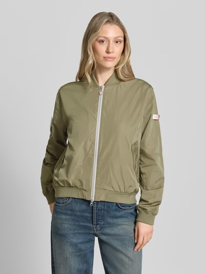 Frauenmodel trägt Bomberjacke mit Label-Patches Modell 'BROOKLYN NEO' von Frieda & Freddies in Olivgrün, Glanz-Optik, Gerader-Schnitt, Stehkragen, Zweiwege-Reißverschluss, Seitliche Pattentaschen mit Druckknopfverschluss, Gerippte-Abschlüsse, Ganzkörperansicht von vorne, Rückenlänge 49 cm, Schulterbreite 42 cm, Brustweite 55 cm, Ärmellänge 63 cm, Größe 36.