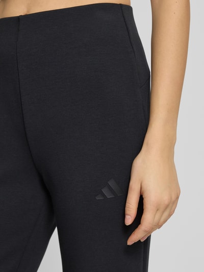 Kobiece model prezentuje Flared Sweatpants mit Logo od adidas Sportswear, czarne, mieszanka modalu, widoczne logo, detal z boku, zbliżenie na biodra.