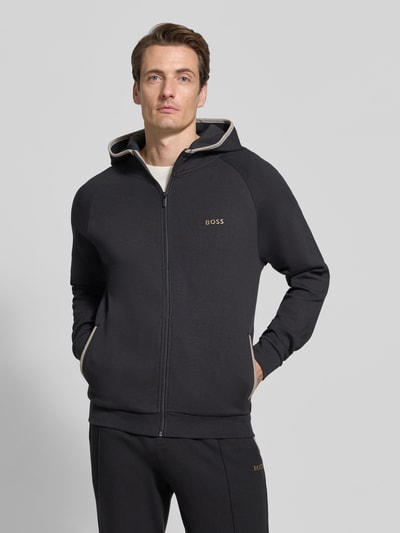 Männermodel trägt Regular Fit Sweatjacke aus Baumwoll-Mix von BOSS in Schwarz mit Kapuze, Reißverschluss und Label-Detail, Nahaufnahme Oberkörper.