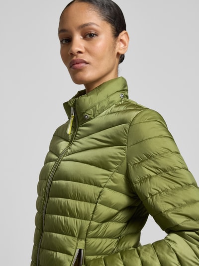 Frauenmodel trägt Steppjacke mit Zweiwege-Reißverschluss von Fuchs Schmitt in Olivgrün, Stehkragen, Reißverschlusstaschen, Nahaufnahme Oberkörper.