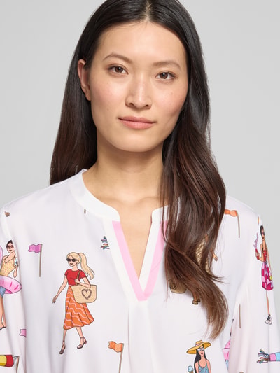 Modelka kobieca nosi Relaxed Fit Tunika-Bluse mit Allover-Motiv-Print od HERZENS, z długim rękawem, dekoltem z lamówką, nadruk z motywem na całej powierzchni, długość tyłu w rozmiarze 36: 70 cm, długość rękawów: 63 cm, jasne kolory, wzory z postaciami, miękka tkanina, zbliżenie na górę sylwetki.