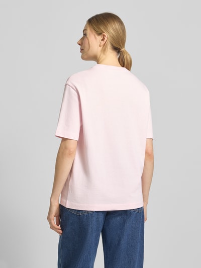 Vrouwenmodel draagt Loose Fit T-Shirt uit zuivere katoen model 'TARJAA' van Armedangels, effen lichtroze, korte mouw, logo-stiksel, fijnrib textuur, ronde hals, Ganzkörperaanzicht achteraan.