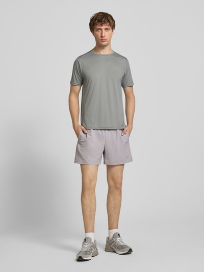 Männermodel trägt Funktionsshirt mit Rundhalsausschnitt und Logo von New Balance in Grau, Regular Fit, glatte Textur, Ganzkörperansicht von vorne.