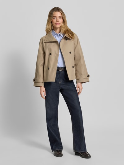 Modelka nosi trencz Trench Jacke mit Bindegürtel Modell 'Munet' od Neo Noir z bawełny, prosty krój, stójka, listwa guzikowa 2-rzędowa, wiązany pasek, patki przy mankietach, wpuszczane kieszenie, długość tyłu w rozmiarze 36: 62 cm, szerokość ramion w rozmiarze 36: 50 cm, szerokość klatki piersiowej w rozmiarze 36: 47 cm, długość rękawów w rozmiarze 36: 56 cm, kolor beżowy, gładka faktura, całopostaciowe zdjęcie z przodu.