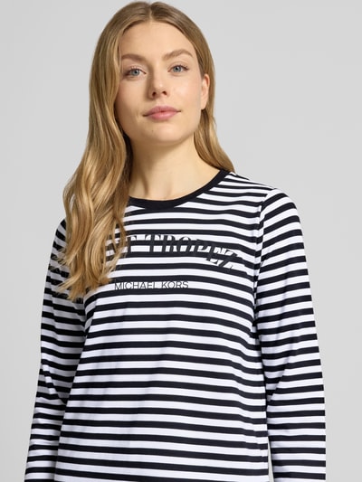 Vrouwenmodel draagt Longsleeve mit Rundhalsausschnitt van MICHAEL Michael Kors in zwart-wit gestreepte katoen met statement-print, rechte fit, pure katoen, halslijn rond, ruglengte maat S 63 cm, close-up bovenlichaam.