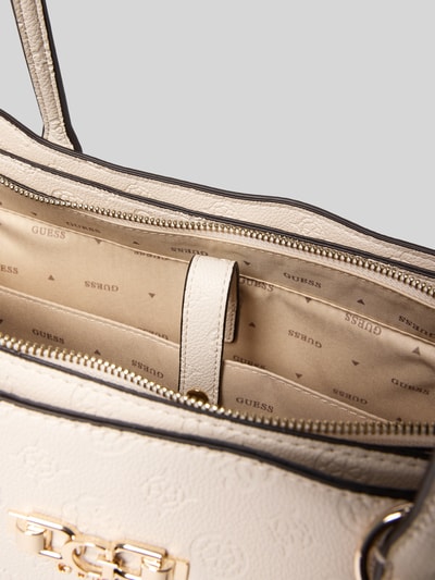 Produktfoto, cremefarbene Handtasche mit Anhänger und Label-Applikation von Guess, Strukturleder, Futter mit Logo, Hauptfach mit Reißverschluss, Detailaufnahme