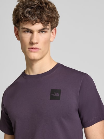 Männermodel trägt T-Shirt aus Baumwoll-Mix Modell 'EVOLUTION' von The North Face in Lila mit Label-Print, Nahaufnahme Oberkörper.