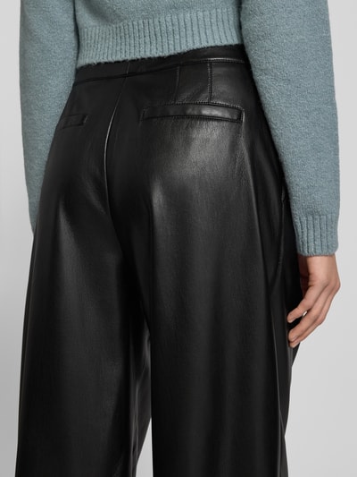Frauenmodel trägt Relaxed Fit Weite Hose mit Bundfalten Modell 'TADESA' von BOSS in glänzender Optik aus schwarzem Kunstleder, Detailaufnahme Rückansicht.