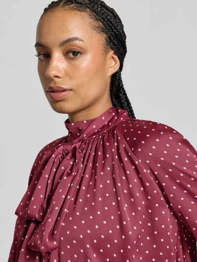 Vrouwenmodel draagt Regular Fit blouse uit satijn van ROTATE, opstaande kraag, sierstrik, langemouwen, ruglengte maat 36: 70 cm, mouwlengte maat 36: 63 cm, bordeauxrood met kleine witte stippen, nahaufnahme bovenlichaam.