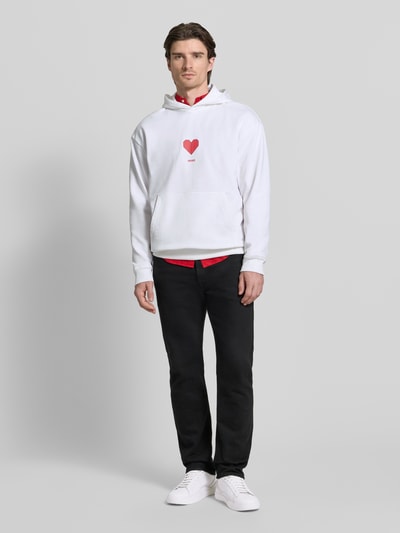 Männermodel trägt Regular Fit Hoodie aus reiner Baumwolle Modell 'DALENTINOS' von HUGO, unifarben weiß, Kängurutasche, Motiv-Print, Ganzkörperansicht von vorne.