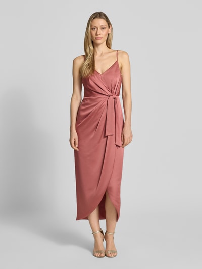 Frauenmodel trägt Regular Fit Midikleid mit verlängerter Rückseite von Jake*s Cocktail aus Satin in Altrosa mit Wickel-Optik, V-Ausschnitt, Spaghetti-Träger, Nahtreißverschluss und Raffungen, Ganzkörperansicht von vorne. Rückenlänge bei Größe 36: 130 cm, Brustweite bei Größe 36: 34 cm.