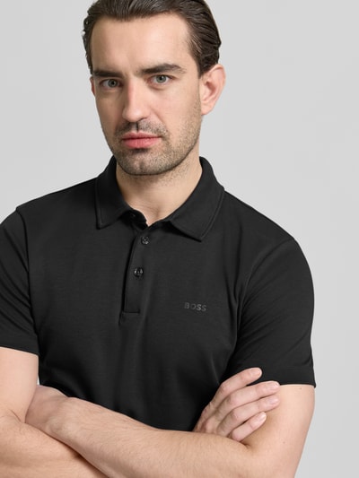 Männermodel trägt Poloshirt mit Brand-Schriftzug von BOSS in Schwarz, reine Baumwolle, Regular Fit, Nahaufnahme Oberkörper.