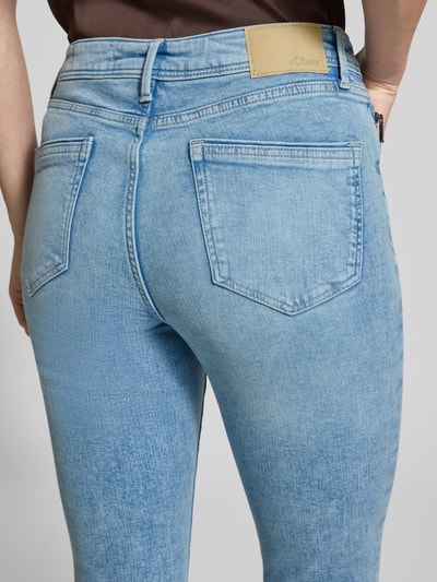 Kobiece modelka nosi Slim Fit Jeans aus Baumwoll-Mix Modell 'BETSY' od s.Oliver RED LABEL o wyglądzie denim, łatka z logo, detaliczne nity, 5 kieszeni, zapięcie na guzik i ukryty zamek, krój slim fit, mieszanka bawełny; jasnoniebieski, gładka tekstura, widok na cały tył.