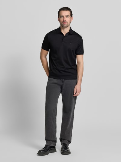 Männermodel trägt schwarzes Poloshirt mit kurzer Knopfleiste von Emporio Armani, Lyocell-Baumwoll-Mix, Regular Fit, Ganzkörperansicht von vorne.