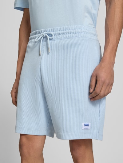 Mężczyznamodel nosi Regular Fit Sweatshorts aus Baumwoll-Mix Modell 'NUWAFFLO' od HUGO w jasnoniebieskim kolorze, bawełniana tekstura, elastyczny pas z troczkiem, naszywka z logo, boczne kieszenie, krój regular fit, kontekst: szorty męskie z bawełnianej mieszanki, widok z przodu, zbliżenie na dolną część tułowia.