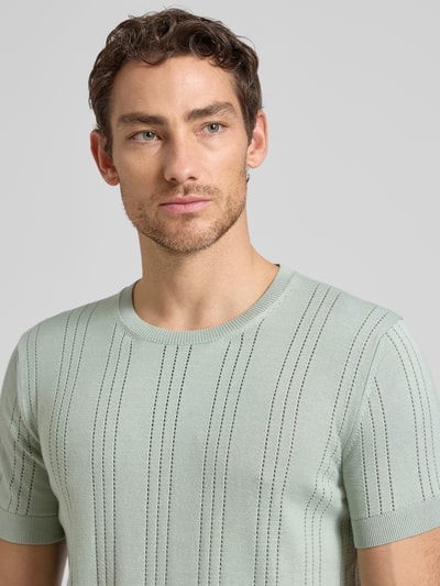 Männermodel trägt Strickshirt aus Viskose-Baumwoll-Mix Modell 'LINDON' von Guess in Pastellgrün, Slim-Fit, Rundhalsausschnitt, Nahaufnahme Oberkörper.