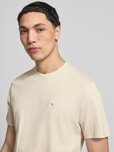 Männermodel trägt T-Shirt mit Label-Badge von Calvin Klein Jeans in Beige, Reine Baumwolle, Regular-Fit, Rundhalsausschnitt, Nahaufnahme Oberkörper.