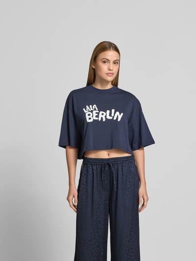 Frauenmodel trägt Cropped T-Shirt mit Logo-Print von Lala Berlin aus Reine Baumwolle, Cropped Fit, Rundhalsausschnitt, Halbarm, Ganzkörperansicht von vorne.