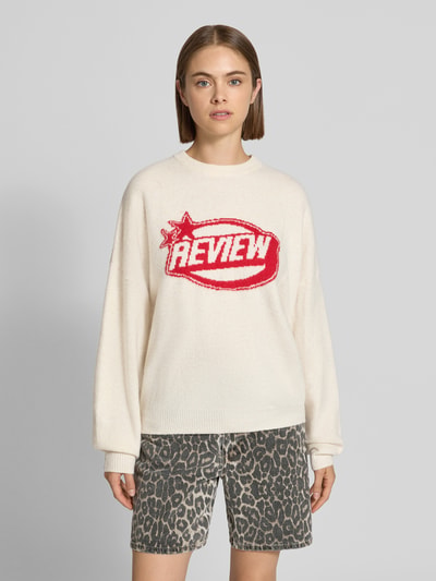 Frauenmodel trägt Strickpullover mit Label-Print von REVIEW, lockerer Schnitt, Rundhalsausschnitt, creme-rot, Ganzkörperansicht von vorne.