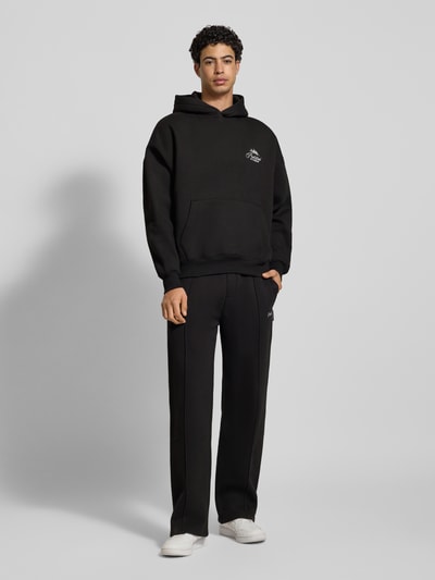 Männermodel trägt Oversized Hoodie mit Label-Stitching von PROHIBITED, schwarz, Baumwoll-Mix, Känguru-Tasche, Gerippte Abschlüsse, Ganzkörperansicht von vorne.