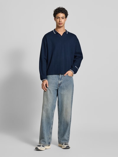 Männermodel trägt Strickpolo aus reine katoen Modell 'JORNIAGARA' van Jack & Jones, V-hals, contrastkraag, elastische mouwboorden, losse fit, labeldetail, donkerblauw, vooraanzicht volledige lichaamsopname.